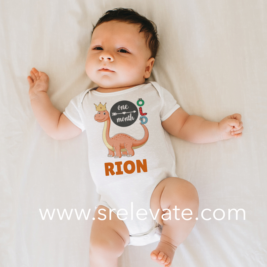 Baby wearing a onesie with a dinosaur design and text, lying on a white surface.