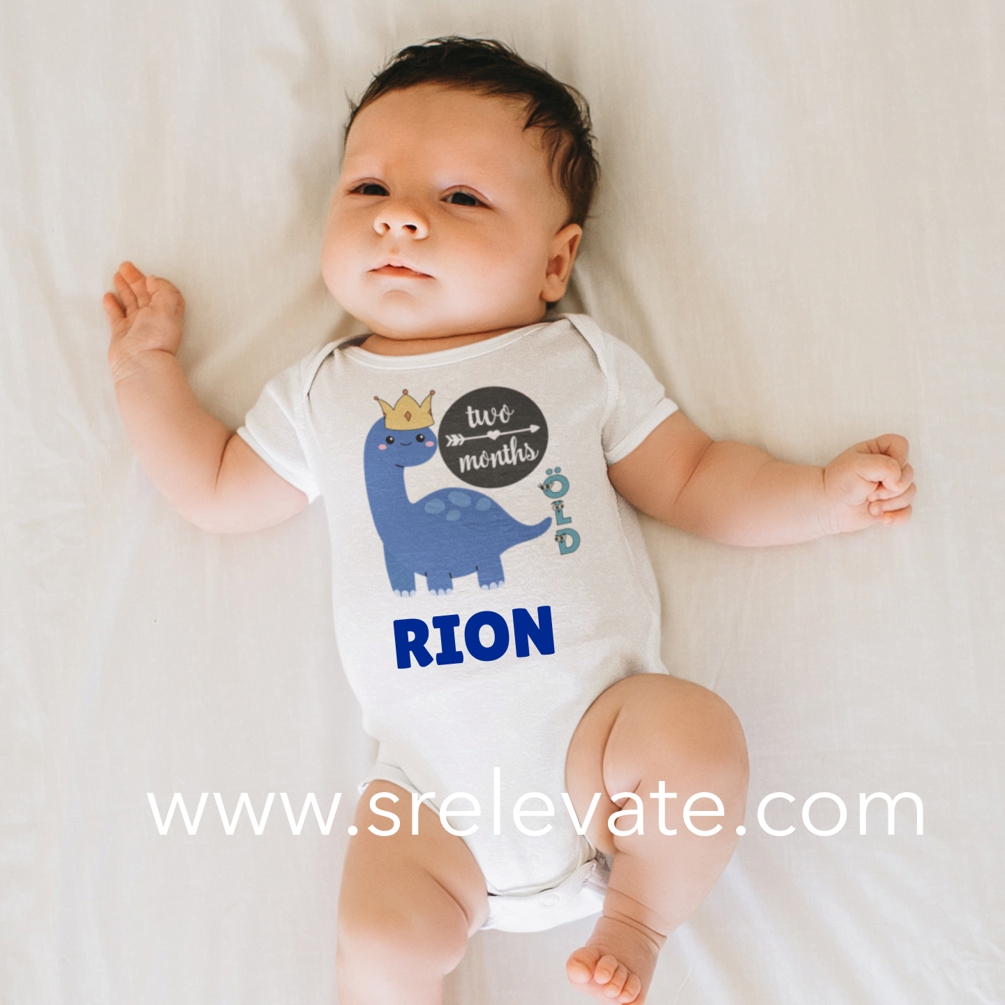 Baby wearing a onesie with a dinosaur design and text, lying on a white surface.