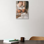 Wall art of a couple holding mugs on a white wall above a table with books and a mug.