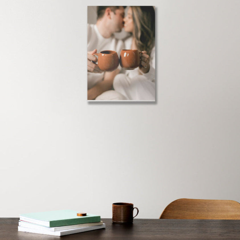 Wall art of a couple holding mugs on a white wall above a table with books and a mug.